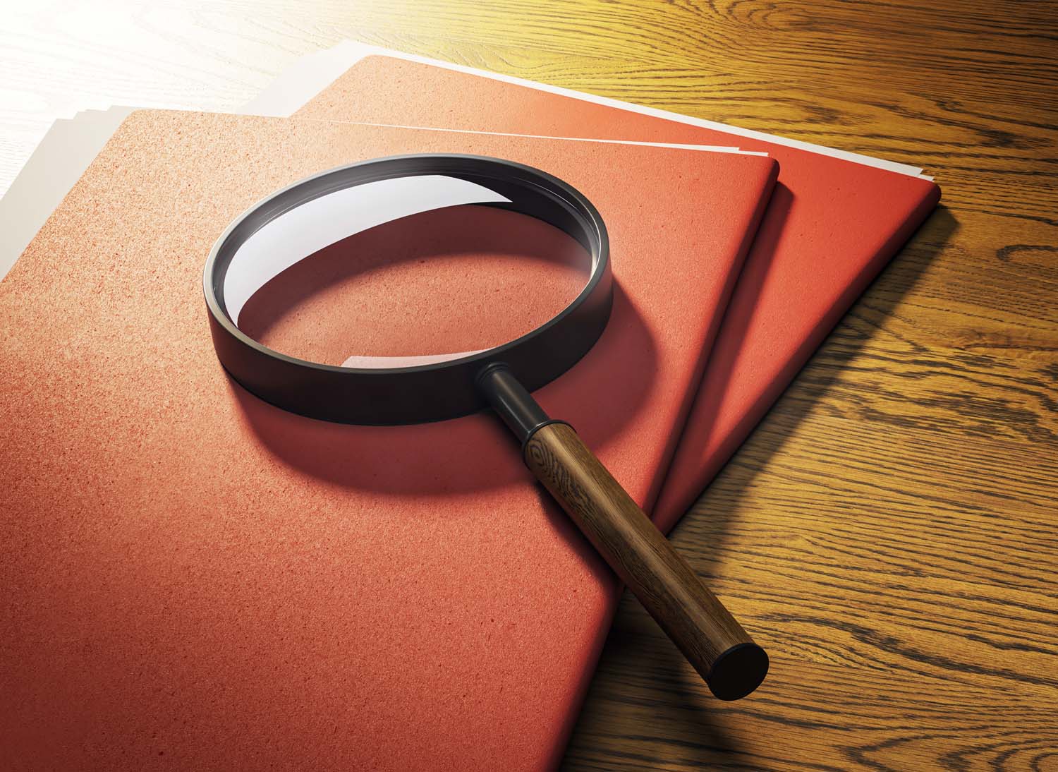 A magnifying glass on top of red folders on a wood table with bright lighting and harsh shadows.